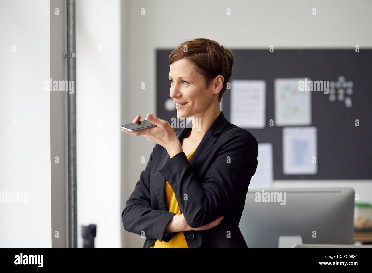 Attractive businesswoman standing in office, using smartphone Banque D'Images