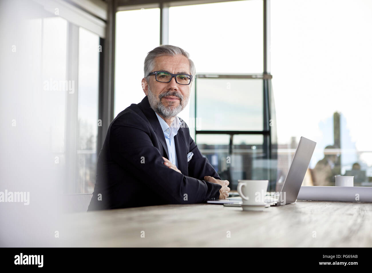 Portrait of smiling businessman with laptop at desk in office Banque D'Images