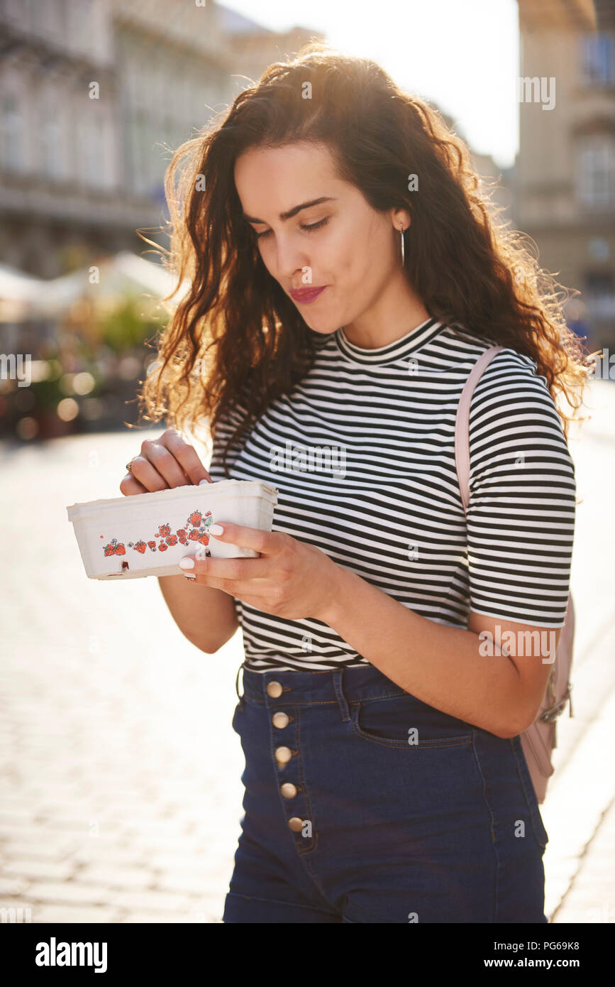 Smiling young woman eating strawberries dans la ville Banque D'Images