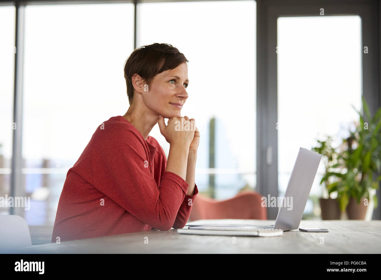 Smiling woman sitting at table at home using laptop Banque D'Images