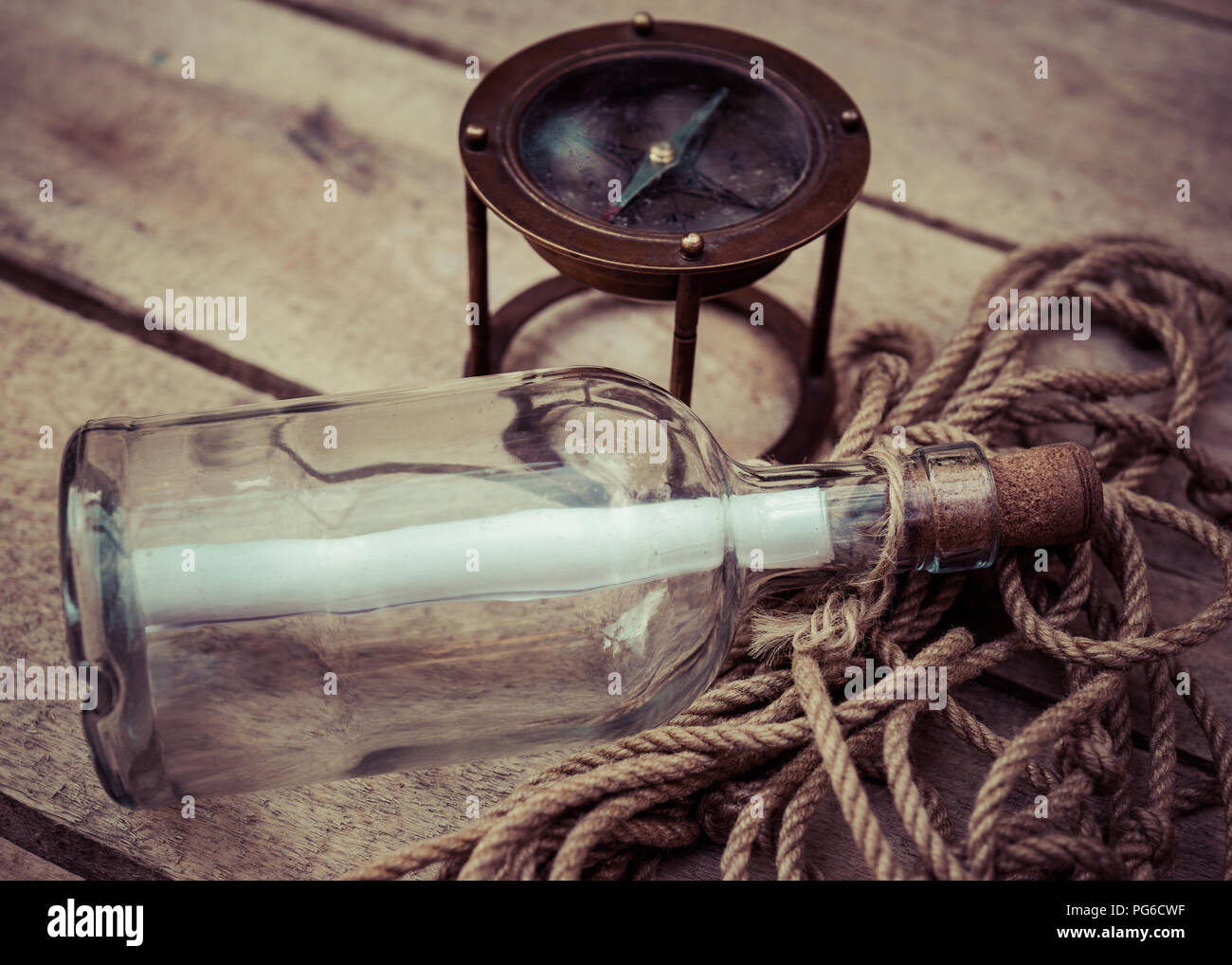 Rouleau de papier blanc à l'intérieur d'une bouteille en verre. Une corde sous la bouteille. Un compas nautique dans l'arrière-plan. Surface en bois. Mail, message, aide et espoir s Banque D'Images