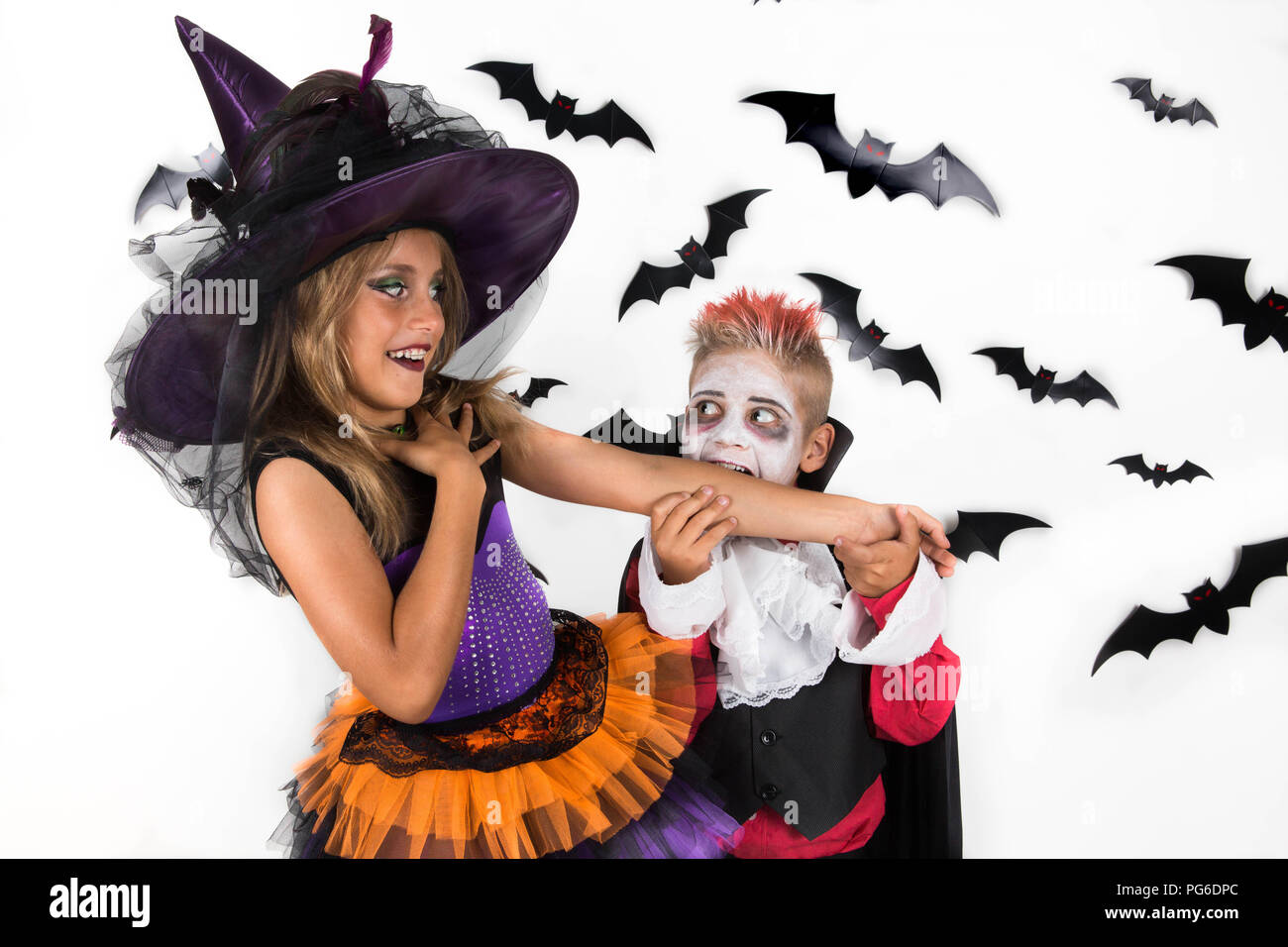 Les enfants font la fête Halloween en costumes de sorcière et de vampire. Vampire fait semblant de mordre le bras de la sorcière et elle sourit en réponse. Banque D'Images