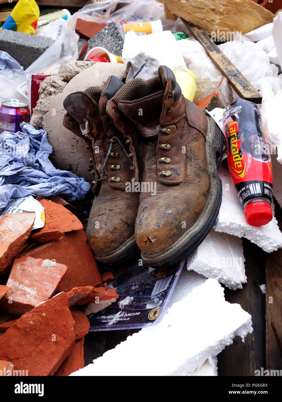 Ancienne paire de bottes des travailleurs jetés dans une thats presque plein constructeurs passer à l'extérieur de l'emplacement de l'édifice Banque D'Images