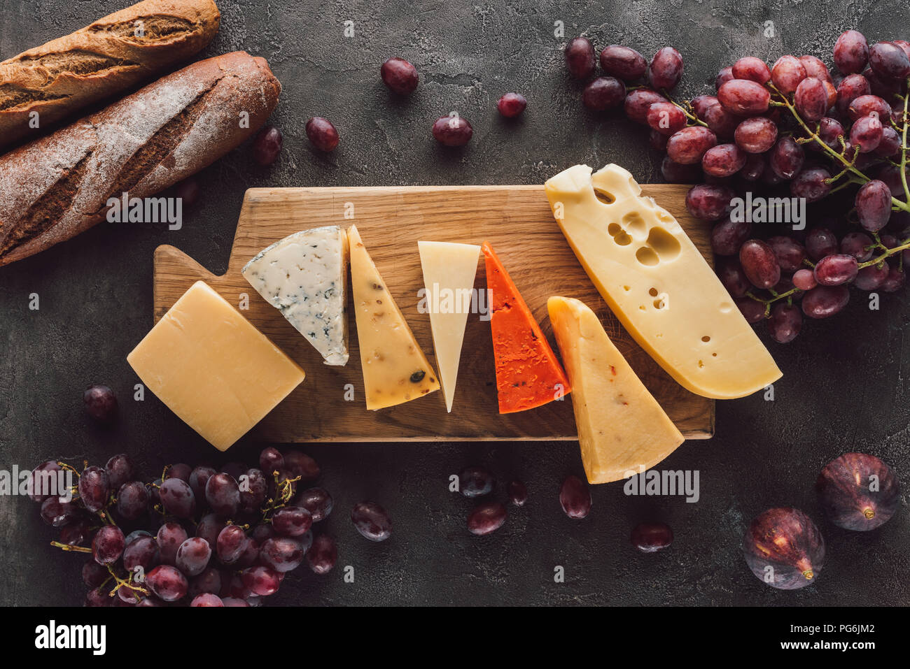Mise à plat avec des baguettes, assortiment de fromages et de fruits sur la table sombre Banque D'Images