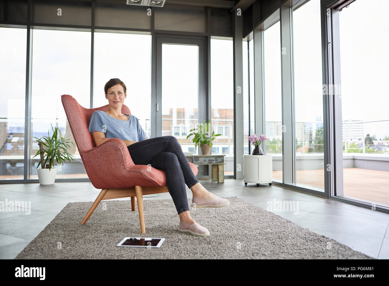 Portrait de femme assise dans un fauteuil à la maison avec à côté de sa tablette Banque D'Images