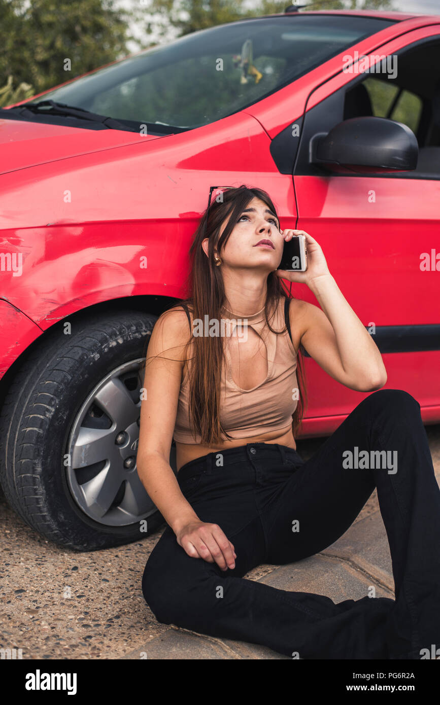 Jeune femme assise au bord de la route ayant une panne de voiture service de dépannage d'appel Banque D'Images