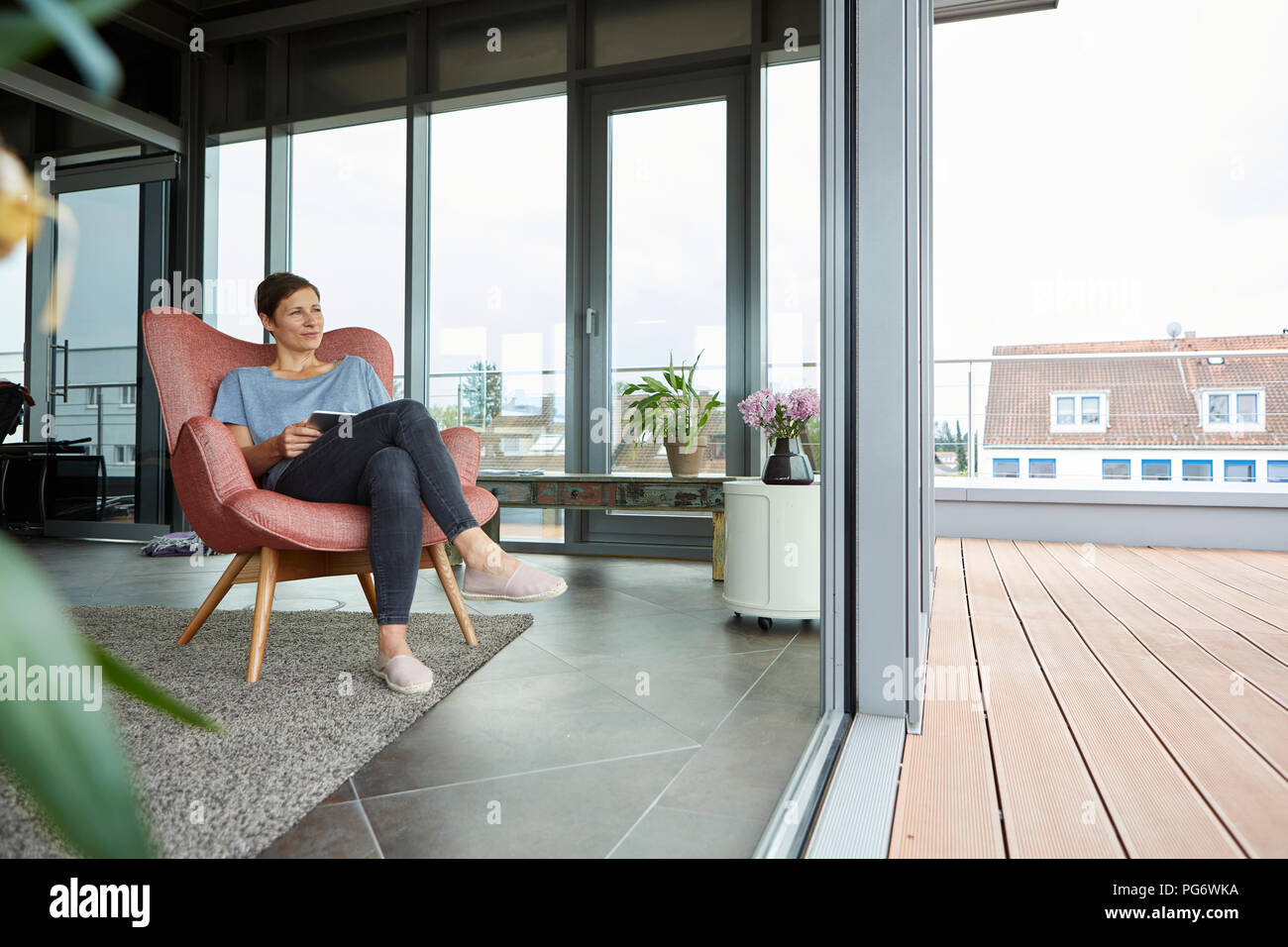 Femme assise dans un fauteuil à la maison avec tablet à la porte du balcon de Banque D'Images