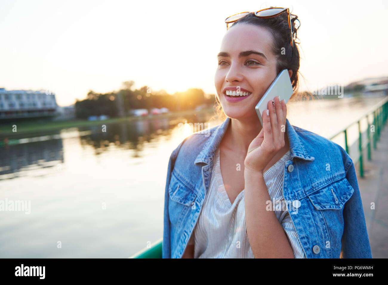 Smiling young woman on cell phone au bord du fleuve au coucher du soleil Banque D'Images