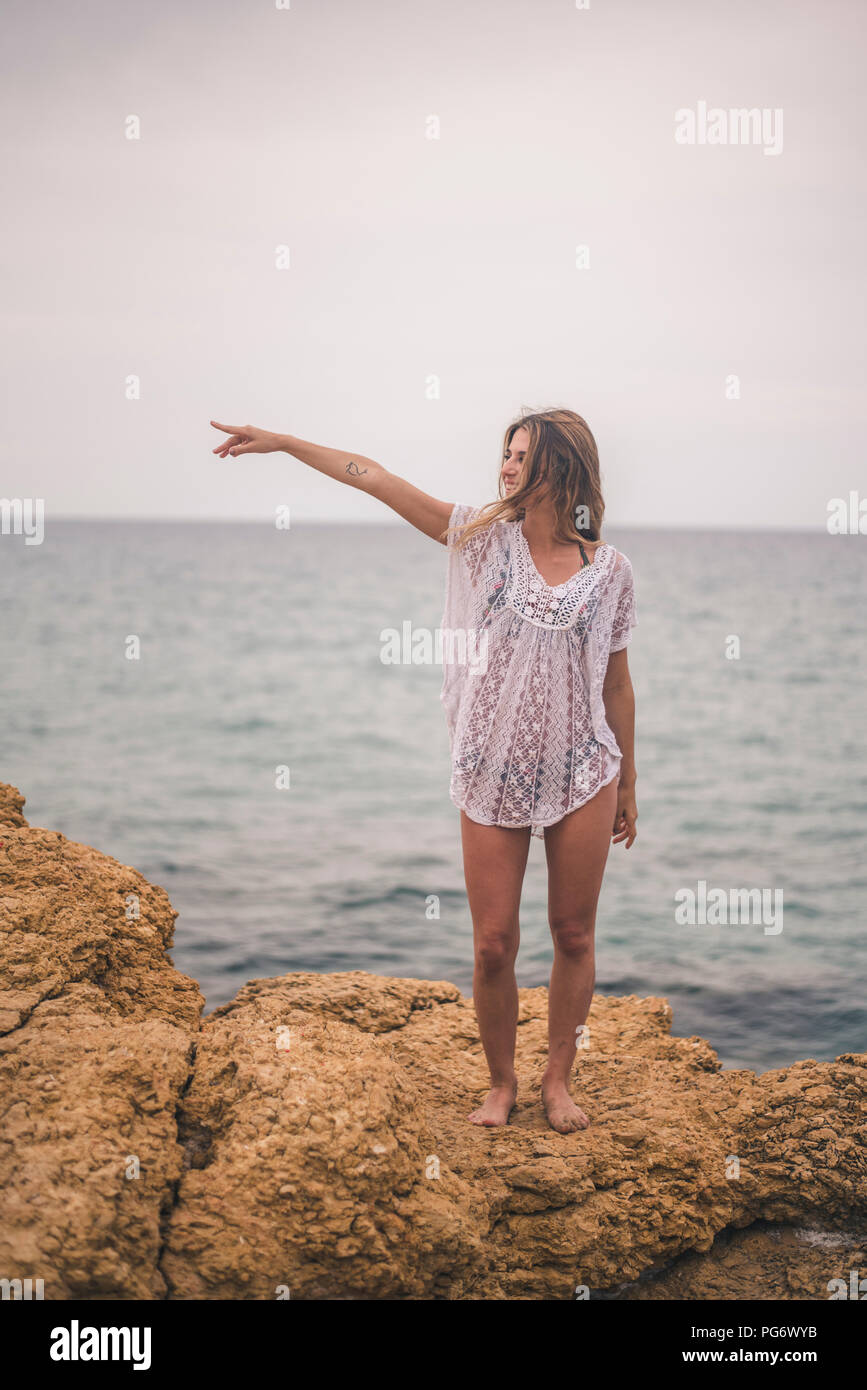 Jeune femme debout sur un rocher à la côte, pointant son doigt Banque D'Images