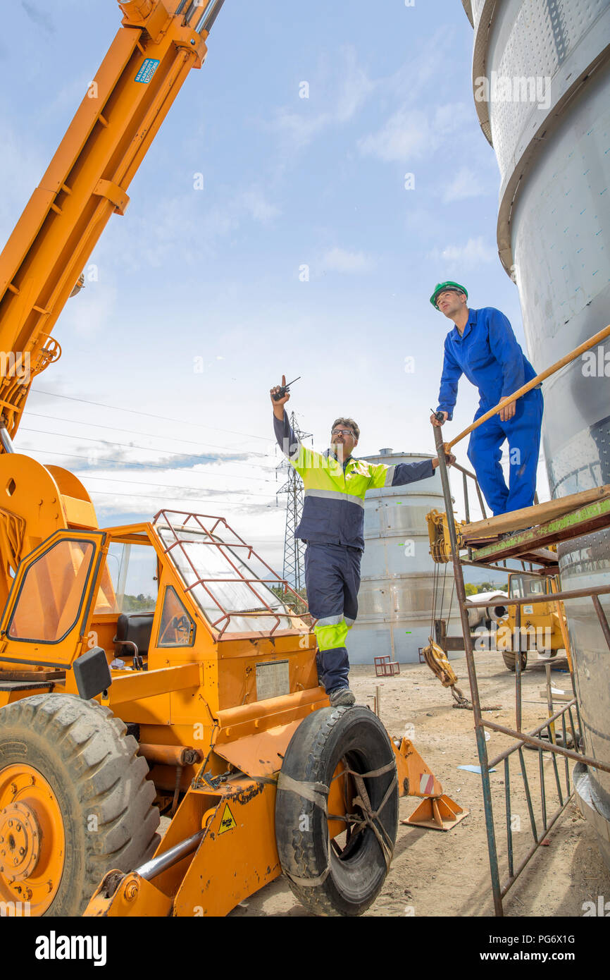 Travailleur de la construction sur le crane de parler à un collègue de travail au niveau du réservoir on construction site Banque D'Images
