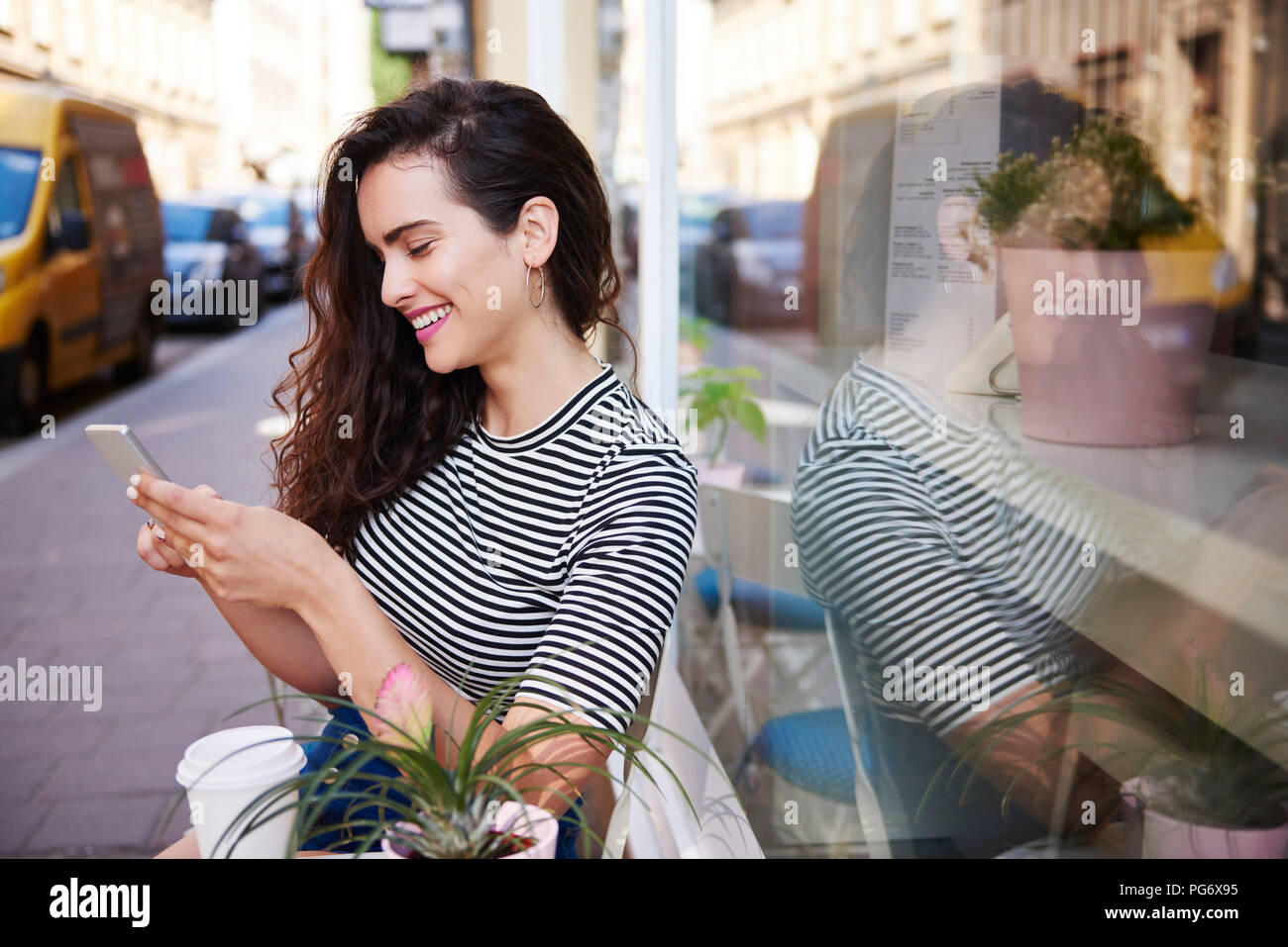 Happy young woman using cell phone at outdoor cafe dans la ville Banque D'Images