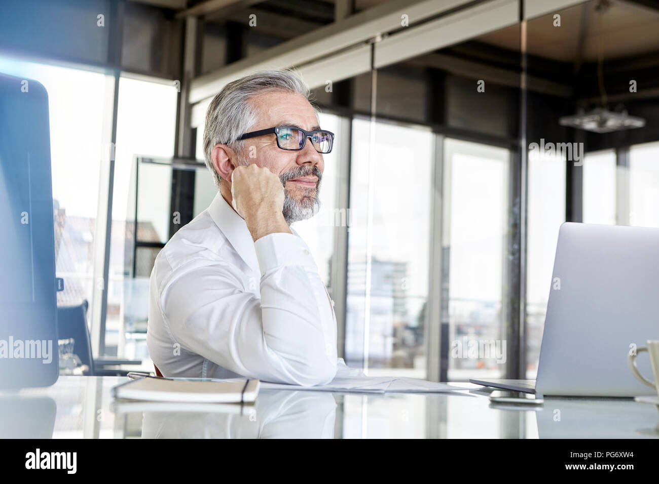 Smiling businessman with laptop at desk in office penser Banque D'Images