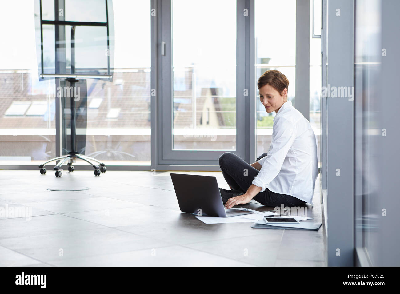 Businesswoman assis sur le plancher d'office à l'aide d'ordinateur portable Banque D'Images