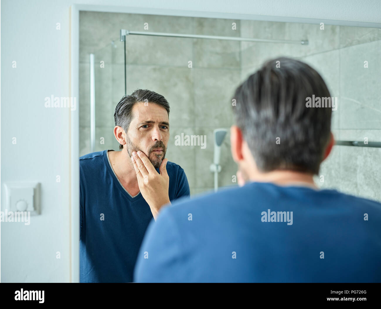 Homme sérieux à la recherche de miroir de salle de bains Banque D'Images