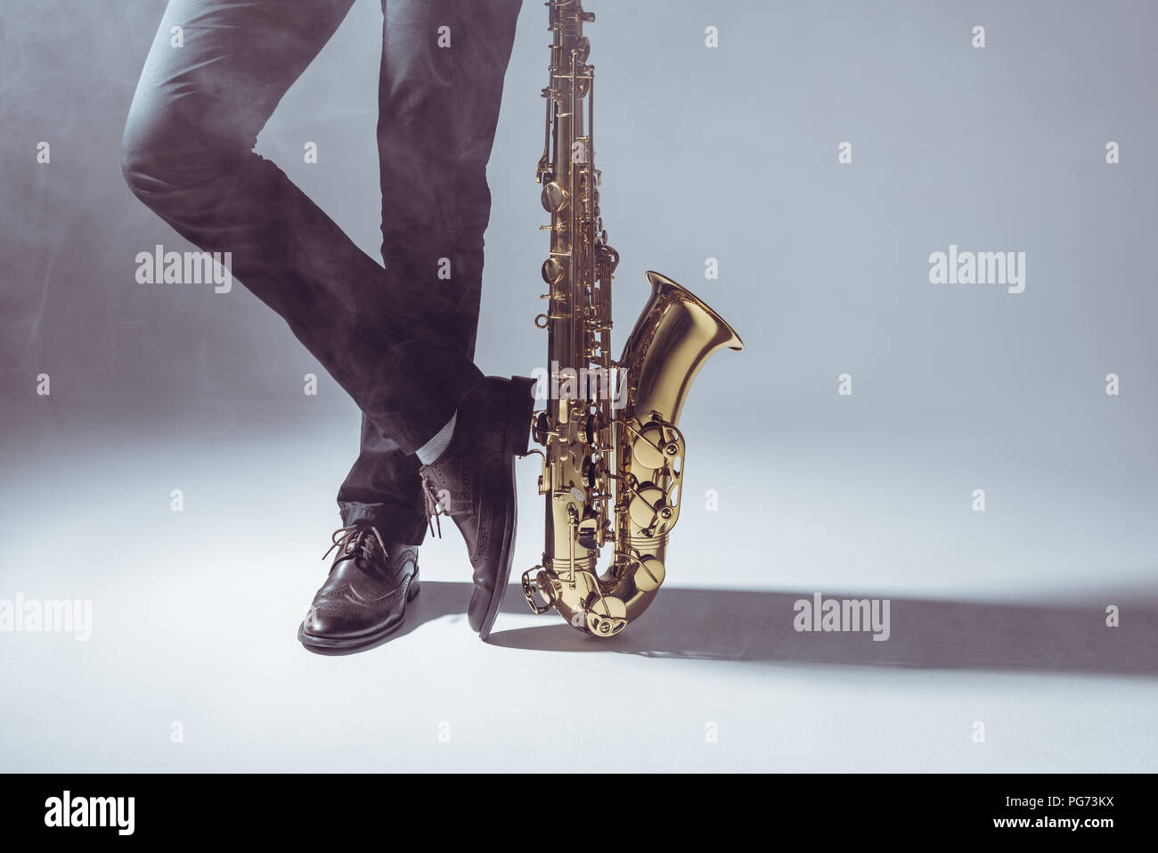 La section basse de musicien professionnel debout avec saxophone dans la fumée sur gray Banque D'Images