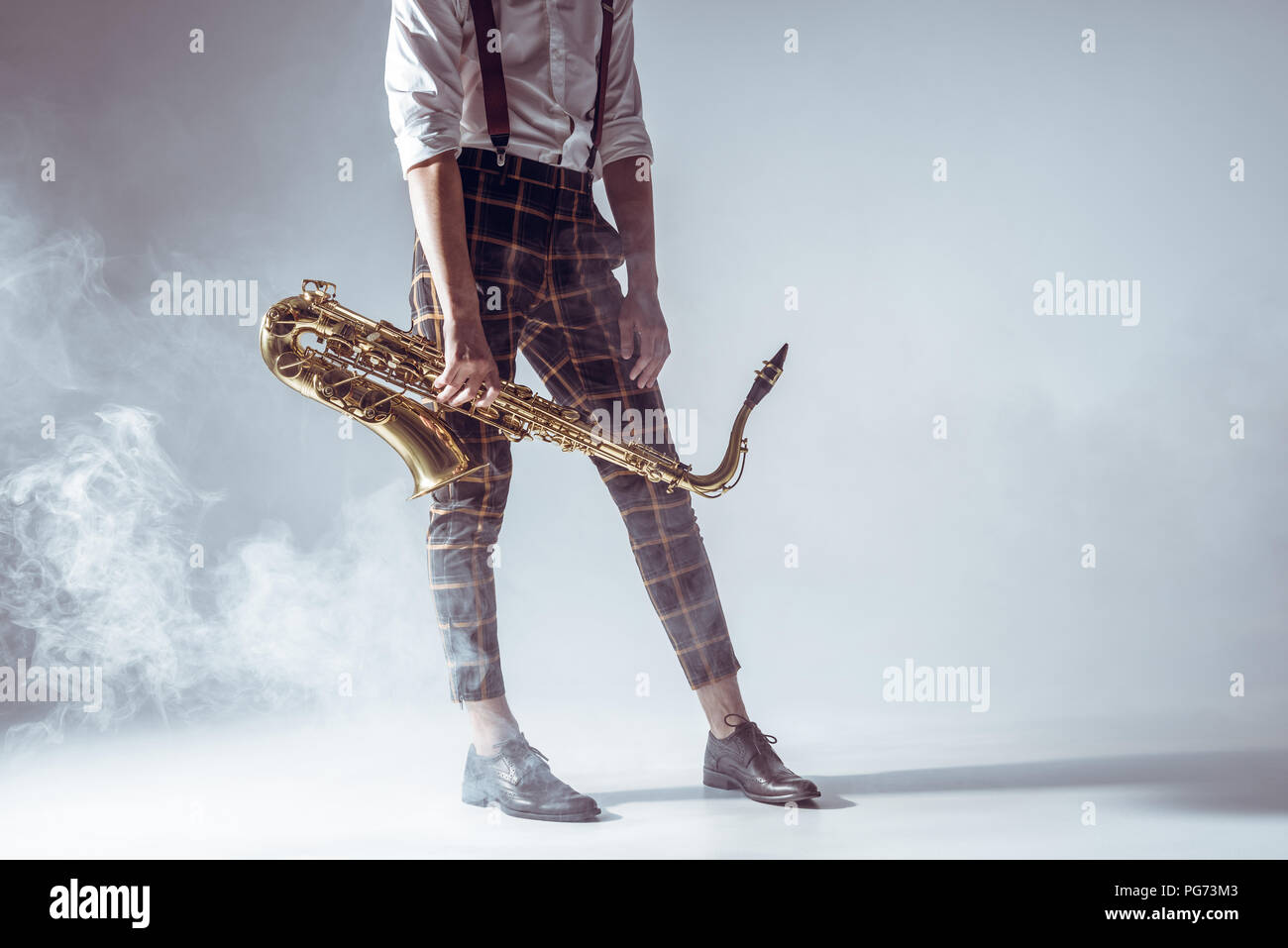 Cropped shot élégant de jeune musicien debout avec saxophone en fumée sur gris Banque D'Images