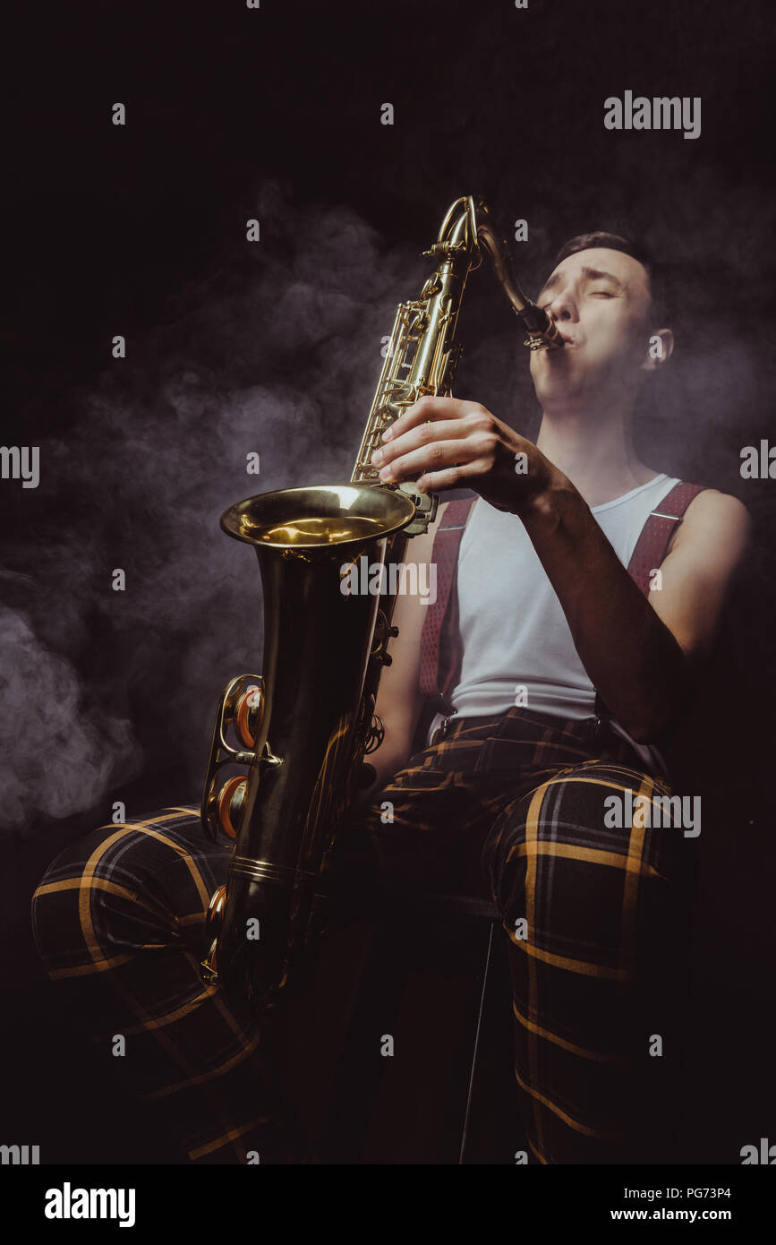 Low angle view of expressive jeune musicien à jouer du saxophone en fumée sur noir Banque D'Images