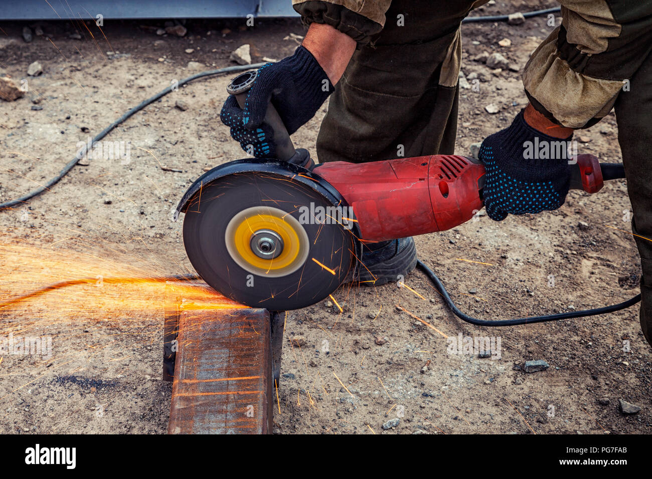 Portrait d'un jeune homme en uniforme brun Soudeur Soudeurs, cuirs, grinder metal une meuleuse d'angle sur le site de construction, orange étincelles voler à th Banque D'Images