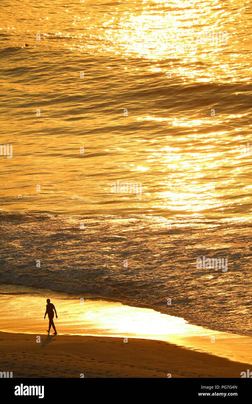 Vue aérienne de l'océan Atlantique dans la lumière du soleil du matin la réflexion avec la silhouette d'un homme marchant sur la plage de Copacabana, Rio de Janeiro du Brésil Banque D'Images