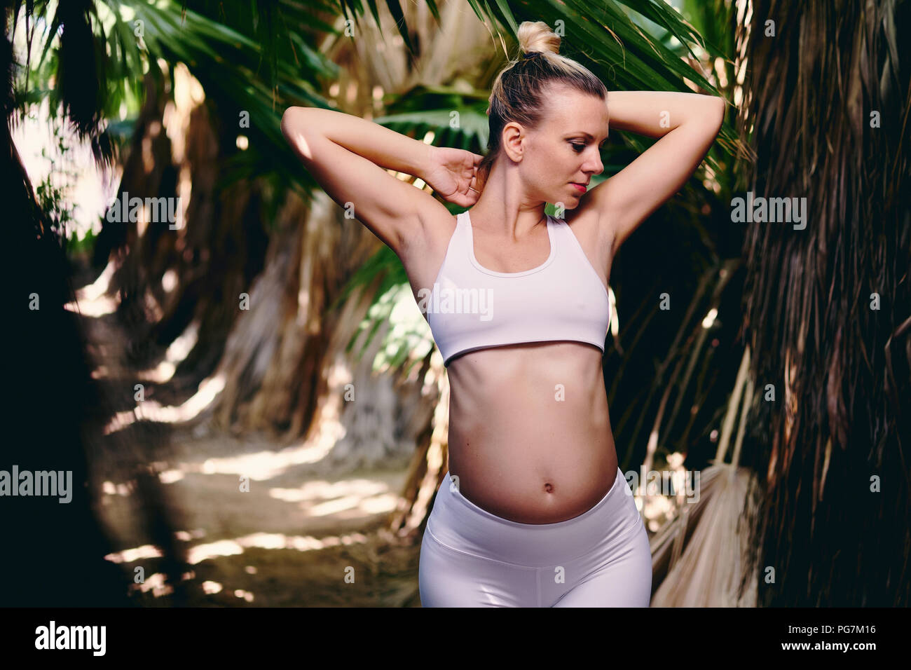 Young attractive blonde woman in white sportswear faisant du yoga pilates exercices de fitness dans la nature tropicale. Avant la naissance de l'exercice, mode de vie sain, rec Banque D'Images