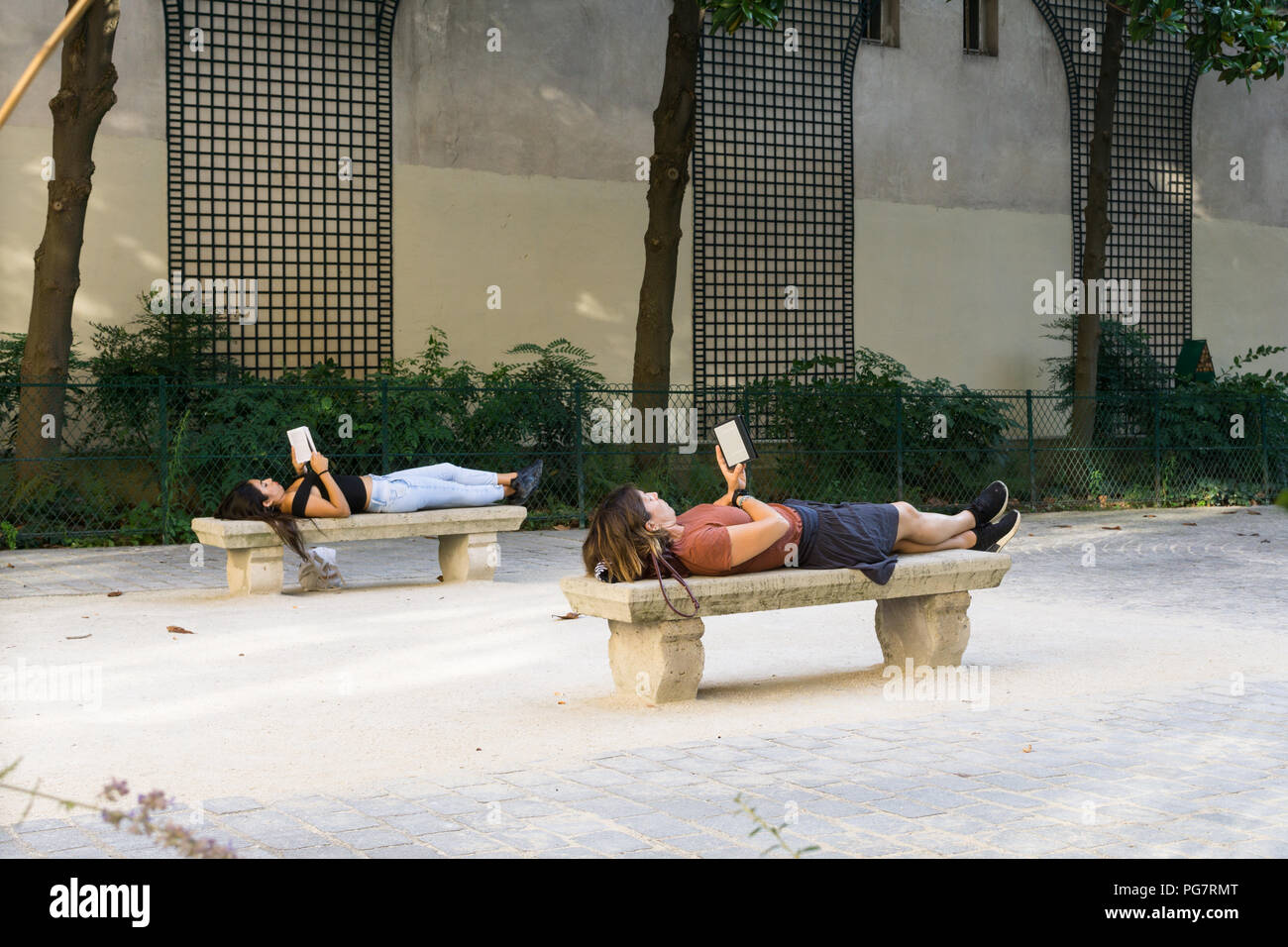 Lecture de livres dans le parc - deux femmes couchés sur des bancs, la lecture de livres à Paris, France, Europe. Banque D'Images