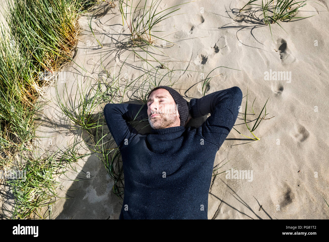 Homme portant woolly hat lying in dune plage Banque D'Images