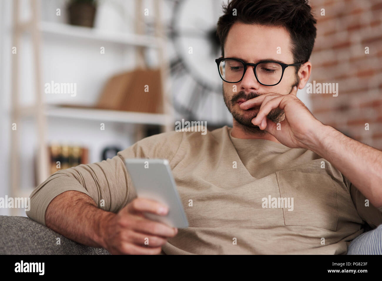 Portrait de l'homme assis sur la table à la maison looking at smartphone Banque D'Images