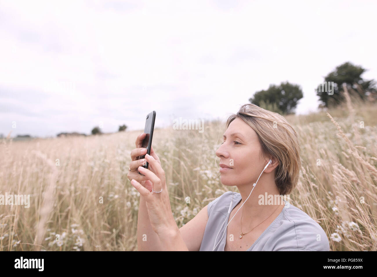 Femme avec écouteurs sur un champ en tenant avec smartphone selfies Banque D'Images