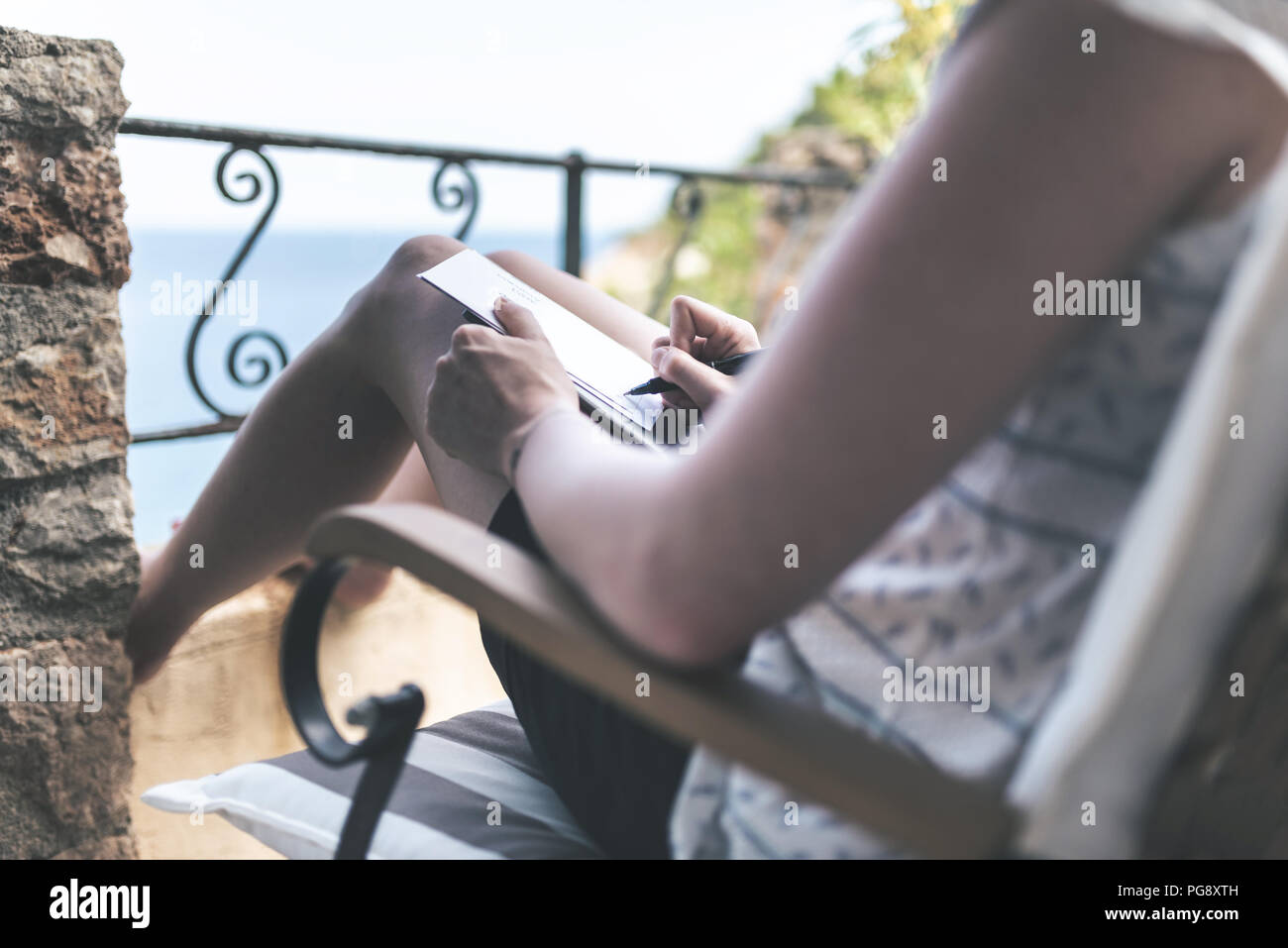 Femme sur patio par mer l'écriture ou la prise de notes avec stylo Banque D'Images