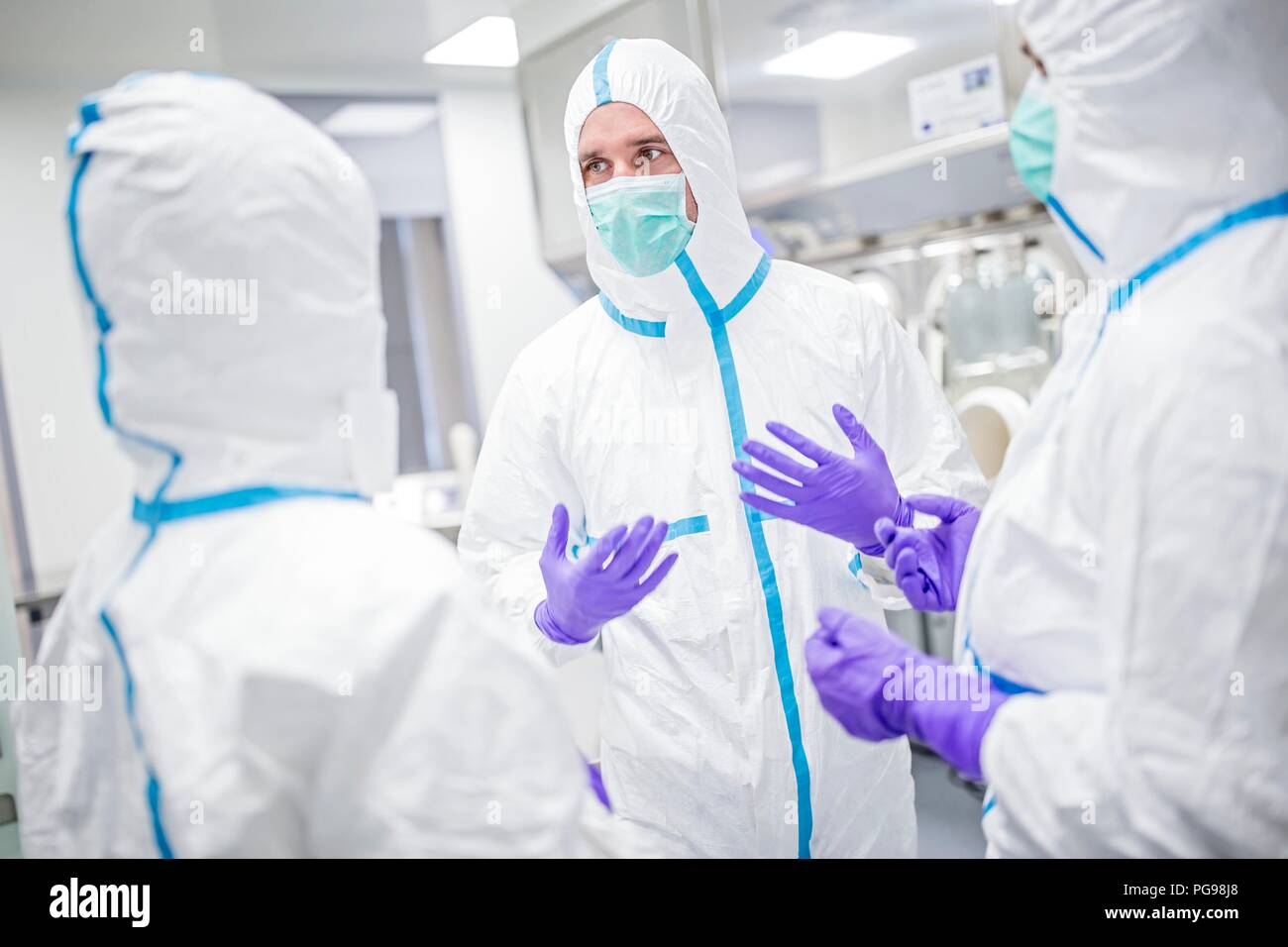 Des techniciens de laboratoires équipés de vêtements de protection et de masques dans un laboratoire qui doit maintenir un environnement stérile. Banque D'Images