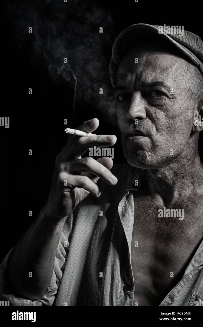 Portrait d'un homme âgé dans un bouchon et avec une cigarette sur un fond sombre . Banque D'Images