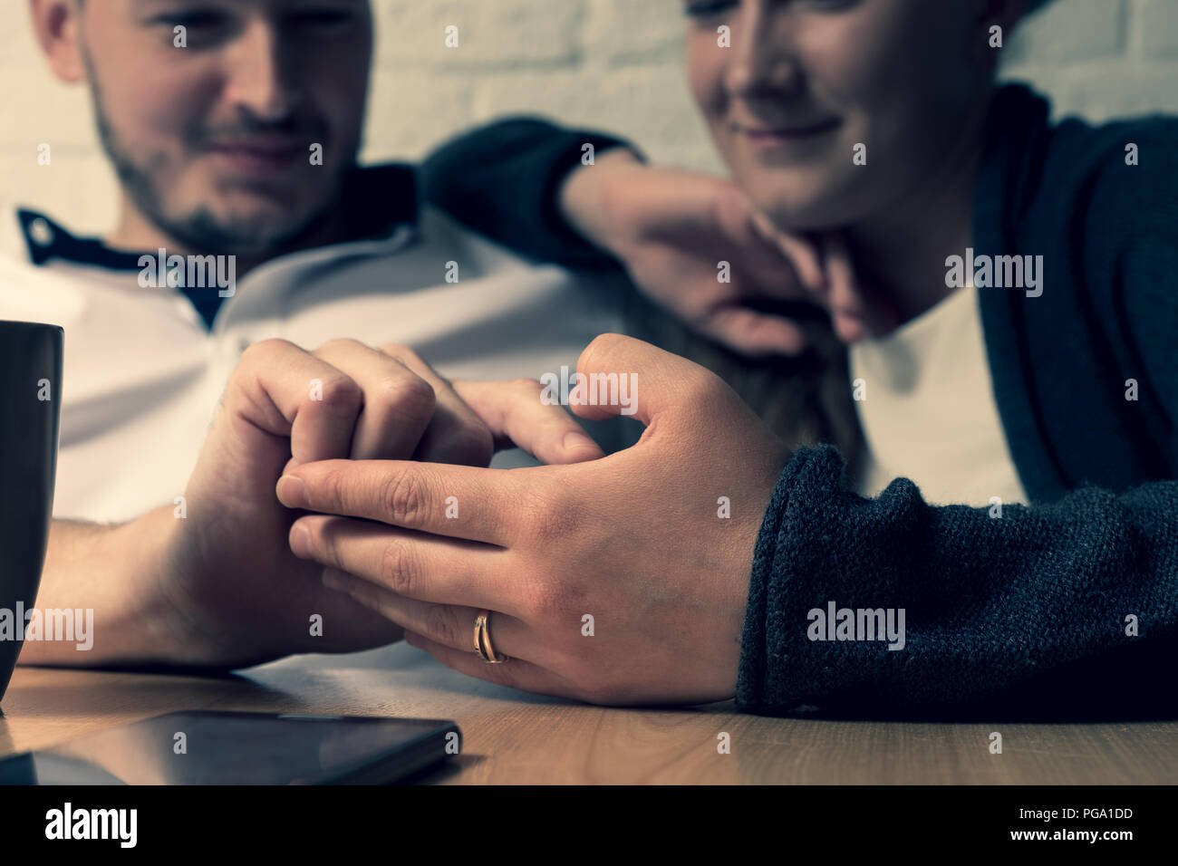 L'homme la main caresse une femme de main. Dans le contexte de l'homme heureux et la jeune fille sont visibles. Devant eux sur une table se trouve le téléphone. La phot Banque D'Images