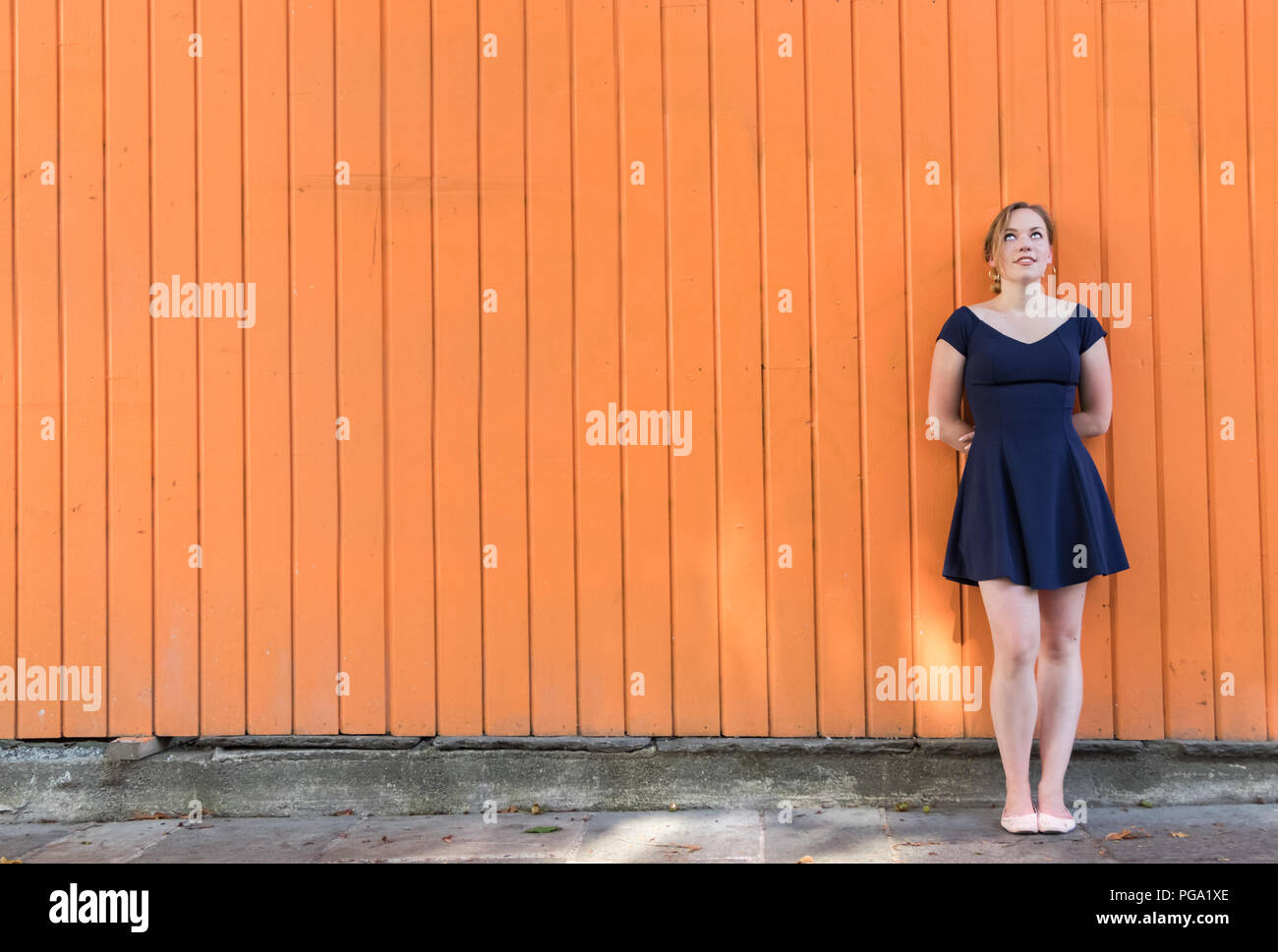 Portrait d'une jeune femme, un corps entier debout sur un mur en bois à l'extérieur dans les rues jusqu'à la réflexion, et de rêver. Banque D'Images