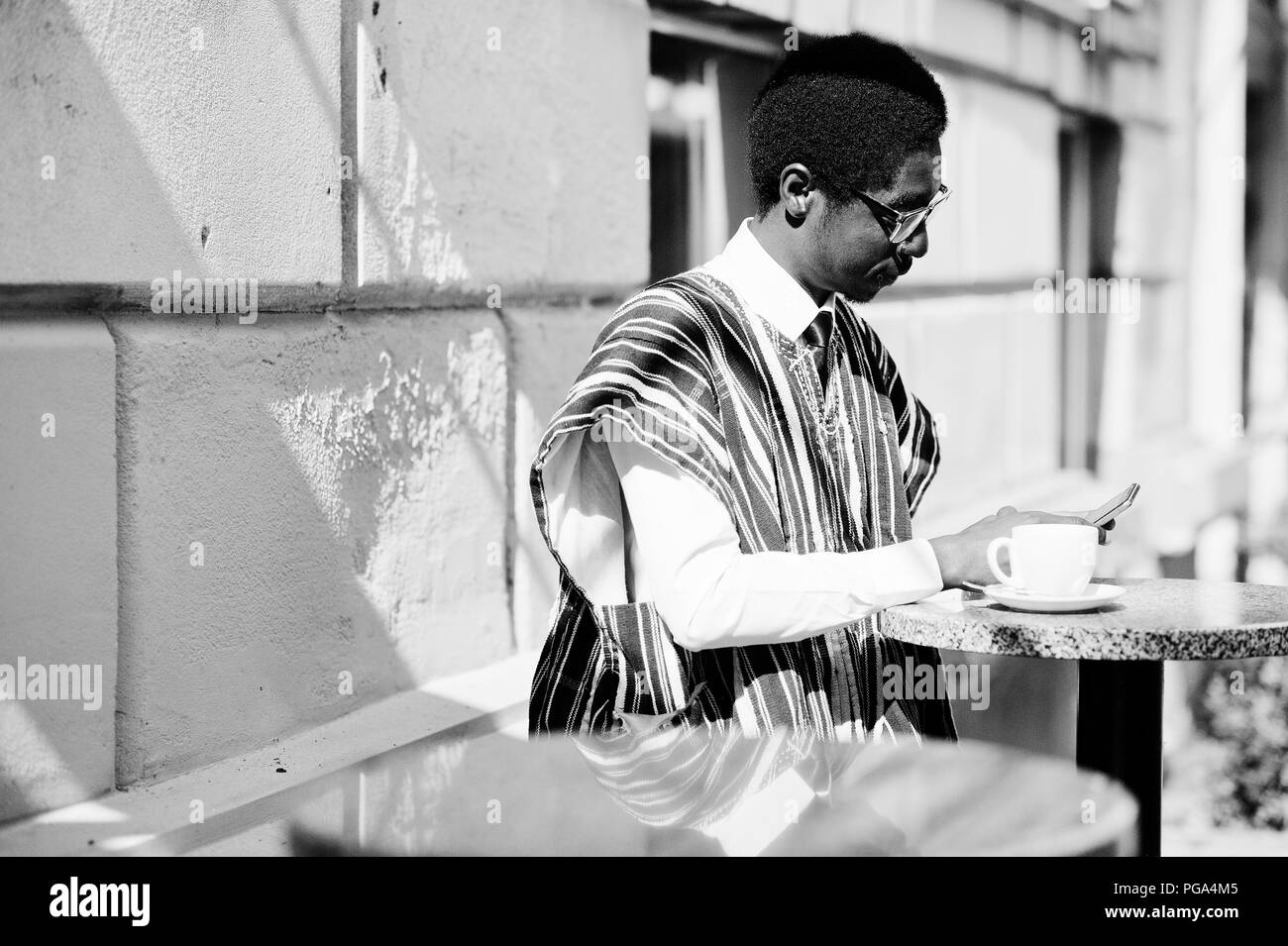 Homme africain en vêtements traditionnels et des verres à café en plein air, boivent du café et à la daily news le téléphone. Banque D'Images
