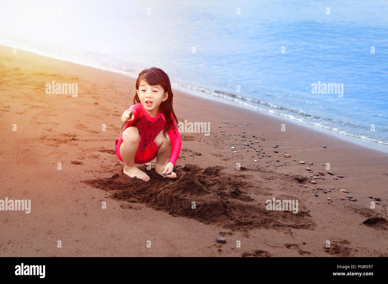 Portrait d'une jeune fille jouant à la plage heureusement pointant à quelque chose Banque D'Images