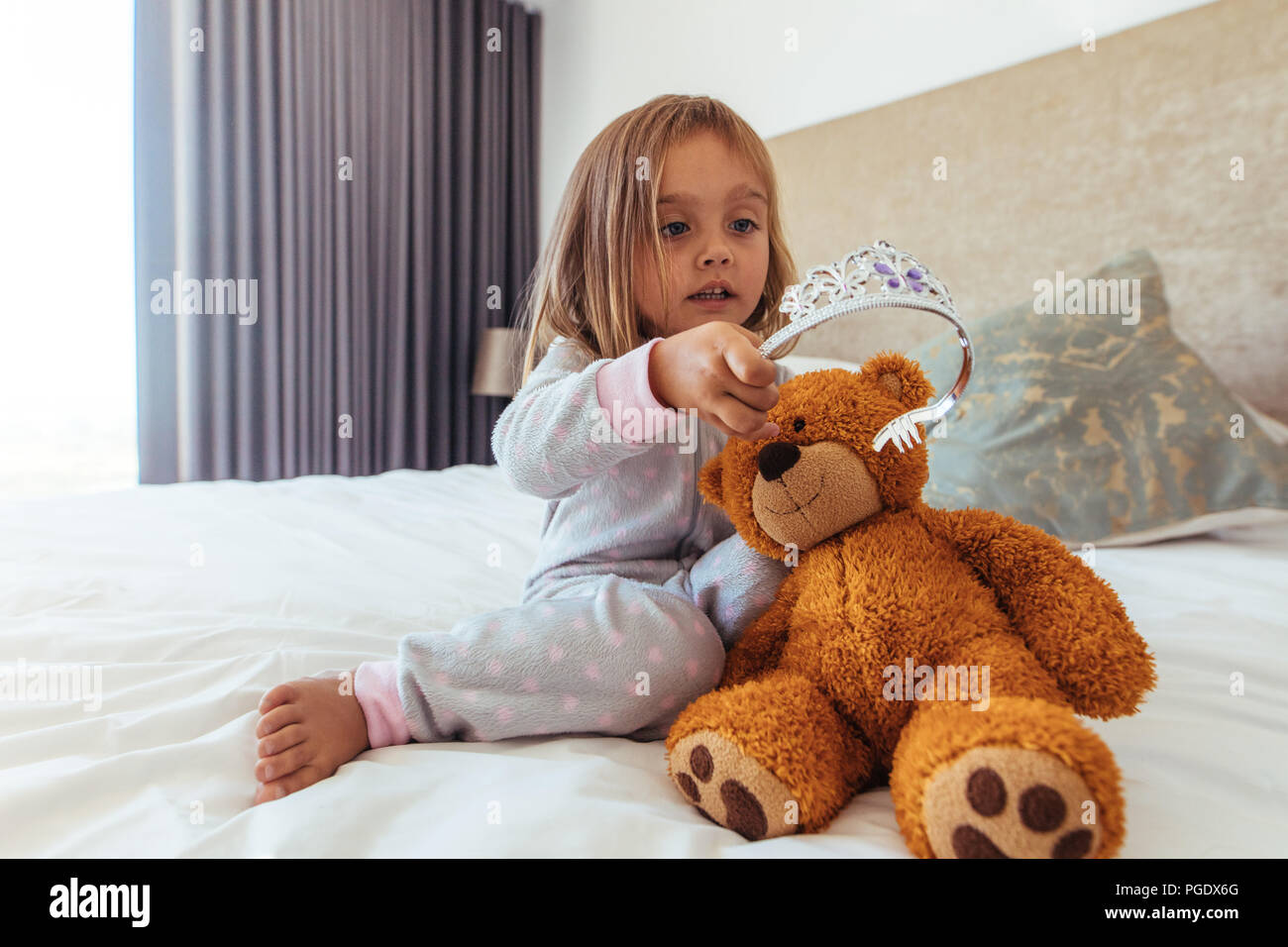 Jeune fille innocente en mettant une couronne sur son ours en peluche. Petite fille jouant avec son doudou. Banque D'Images