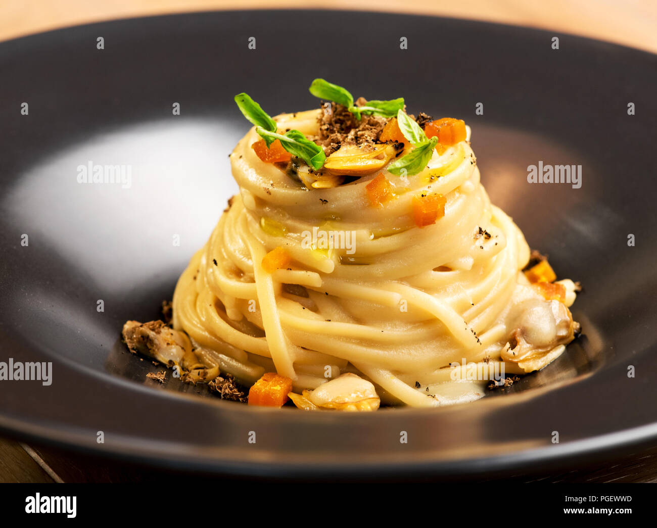 Entrée avec Gourmet pâtes linguine italienne dans une sauce crémeuse, les palourdes et les truffes dans un gros plan Vue de côté dans un bol en céramique noire Banque D'Images