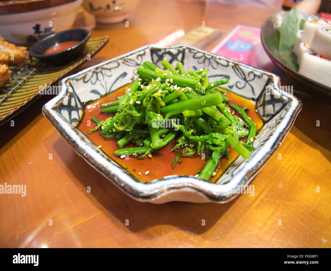 Plaque de cuisson style taïwanais fougère, légumes avec sauce rouge et d'autres plats à l'arrière-plan Banque D'Images