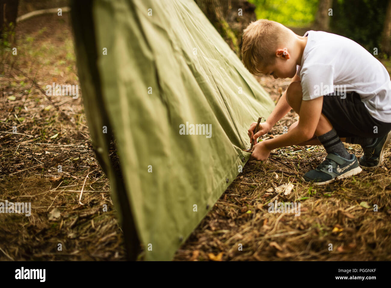 Boy laying poncho pour prendre refuge dans les bois Banque D'Images