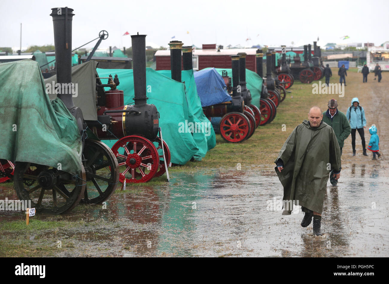 Les visiteurs font leur chemin passé couvert comme moteurs de traction à vapeur d'une douche à effet pluie passe au-dessus de la Grande Vapeur Dorset, juste à Blandford, Dorset, où des centaines de moteurs de traction à vapeur période lourde et l'équipement mécanique de toutes les époques se sont réunis pour la foire annuelle pour célébrer le 50e anniversaire de l'émission. Banque D'Images