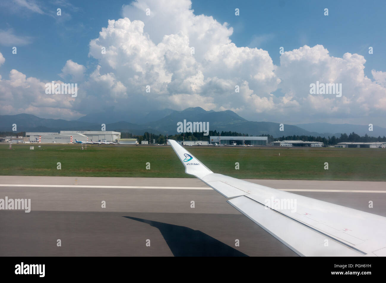 Ljubljana, Slovénie - 25 août 2018 : voir à travers la fenêtre de l'avion sur l'aile d'avion, Adria Airways logo sur l'extrémité de l'aile et Ljubljana Joze Pucnik airpo Banque D'Images