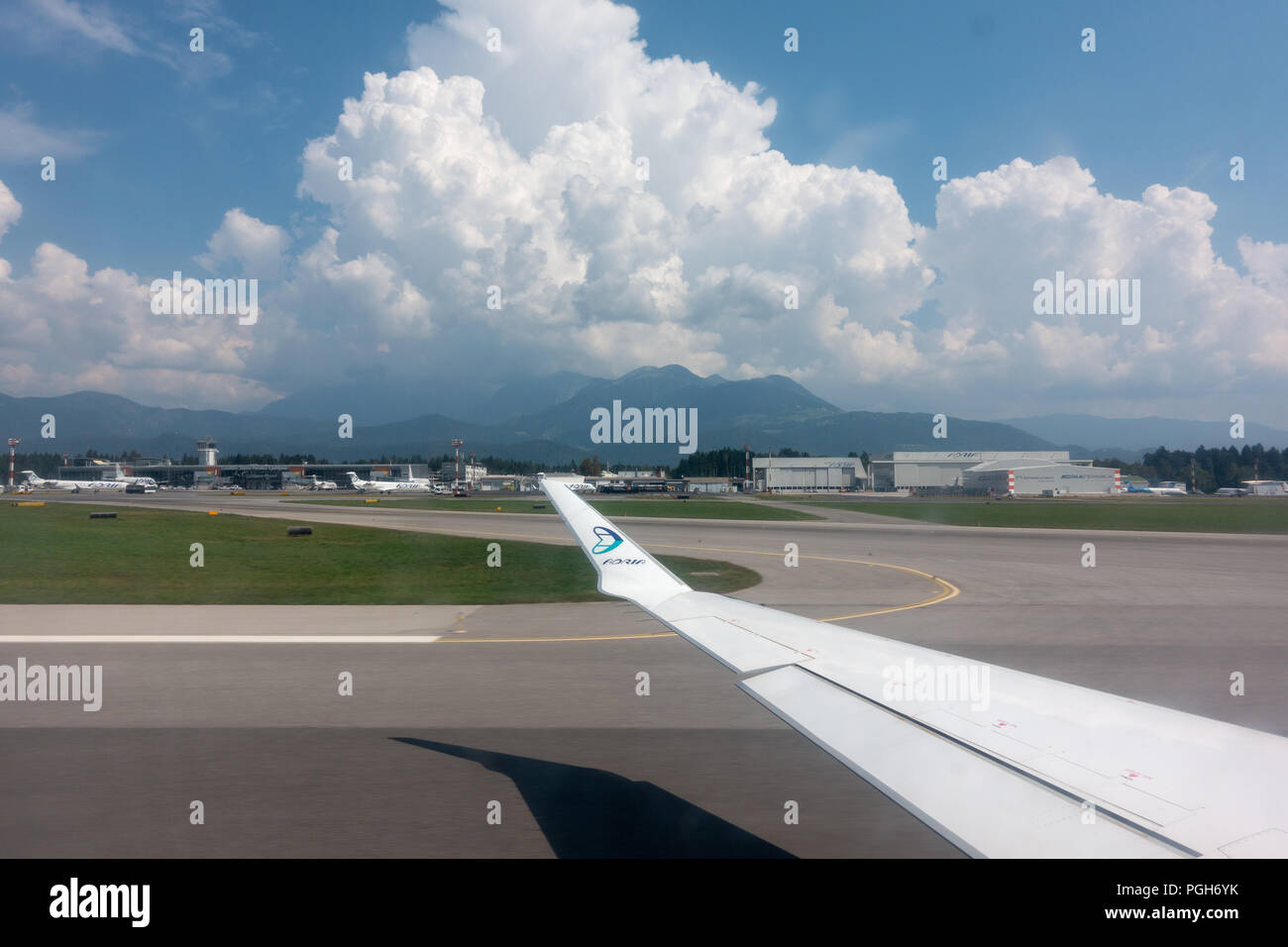 Ljubljana, Slovénie - 25 août 2018 : voir à travers la fenêtre de l'avion sur l'aile d'avion, Adria Airways logo sur l'extrémité de l'aile et Ljubljana Joze Pucnik airpo Banque D'Images