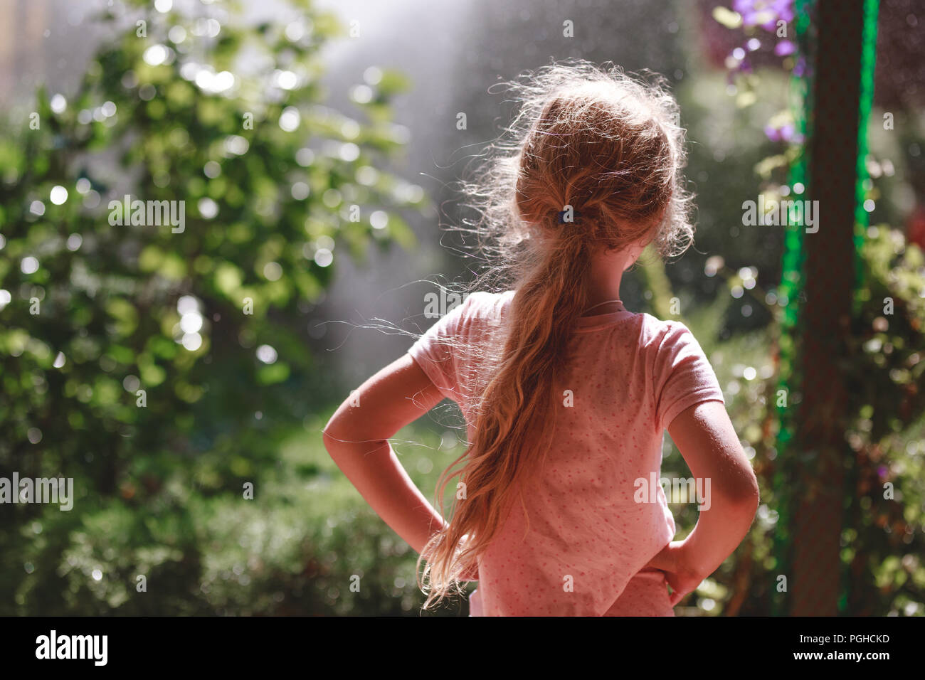 Vue arrière de 7 ans fille blonde wearing pajamas extérieur permanent dans le jardin d'accueil en début de matinée. Banque D'Images