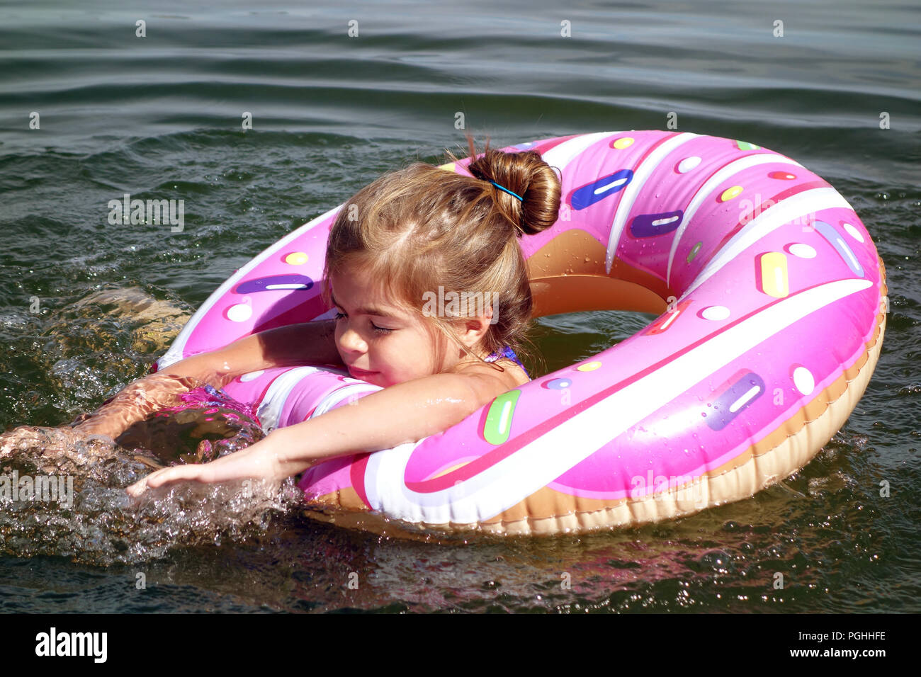 Jeune fille aux cheveux en chignon s'amusant en natation dans le lac naturel rose gonflable donut bague en caoutchouc Banque D'Images