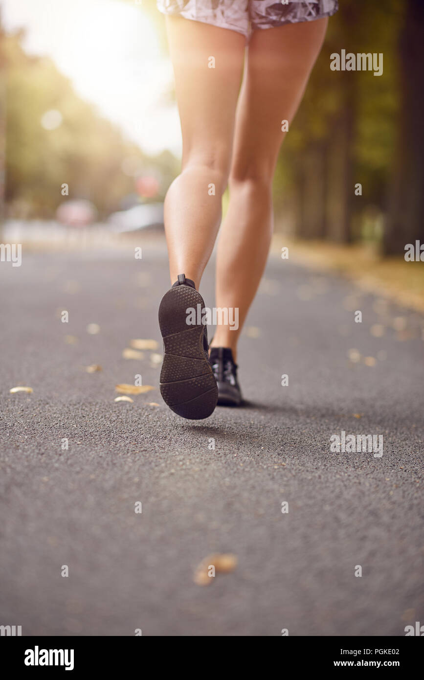 Jeune femme de marche ou de jogging dans une rue d'automne par rétro-éclairé l'éclat du soleil du soir dans un portrait de son gel jambes en short et sable Banque D'Images