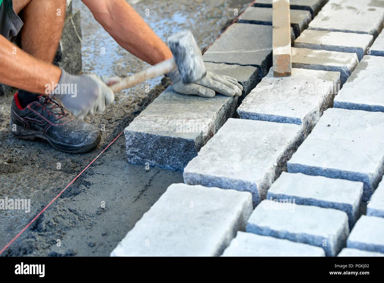 Un ouvrier a les mains gantées utiliser un marteau pour placer les pavés en pierre. La création d'un travailleur à l'aide de blocs et de la chaussée pavée de pierres de granit. Je travailleur industriel Banque D'Images