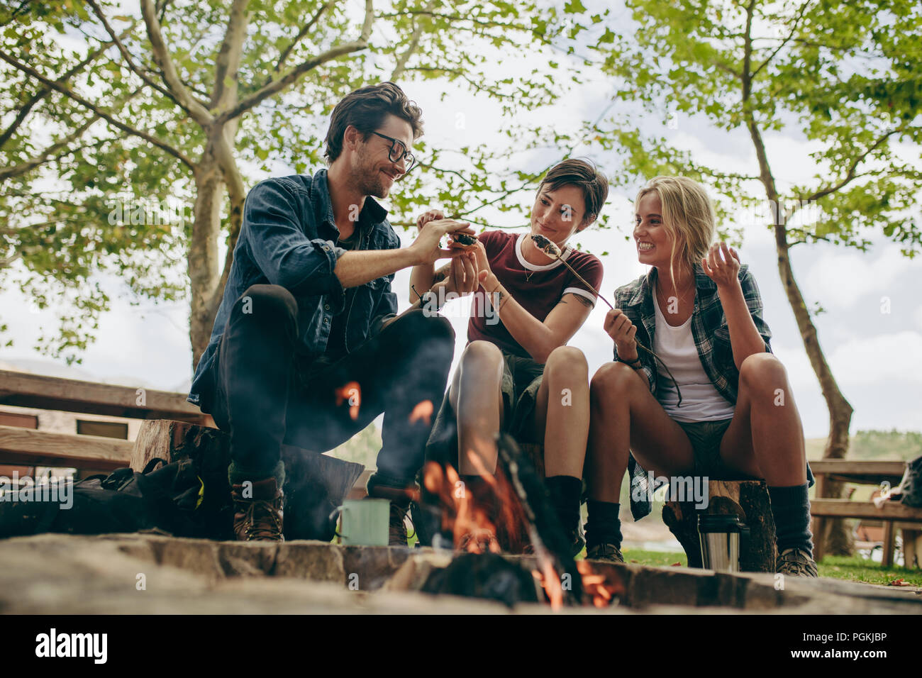 Smiling friends toasting en vacances sur l'alimentation de joie. Les amis de faire un sandwich avec des guimauves grillées assis à l'extérieur dans la campagne. Banque D'Images