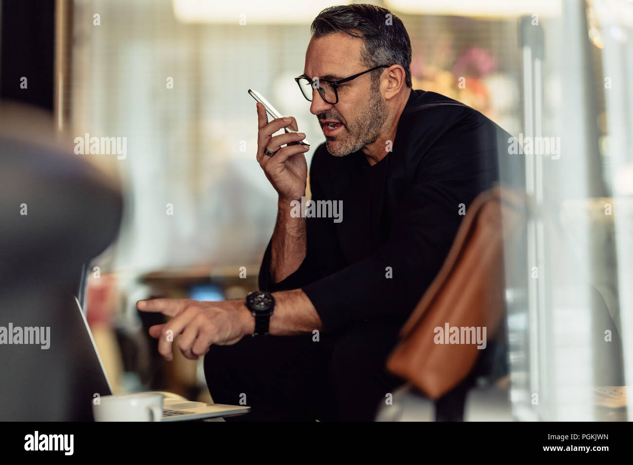 Mature businessman talking on phone while looking at laptop. Chef de groupe alors qu'il était assis dans le hall de l'hôtel. Banque D'Images