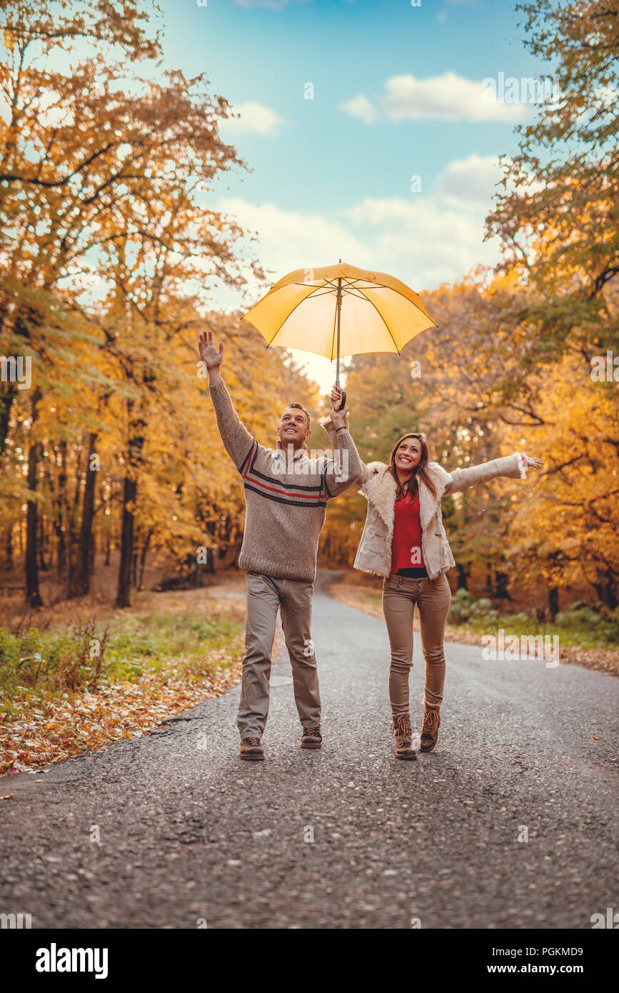 Belle cheerful young couple avec parapluie jaune ayant in sunny park en couleurs de l'automne. Banque D'Images