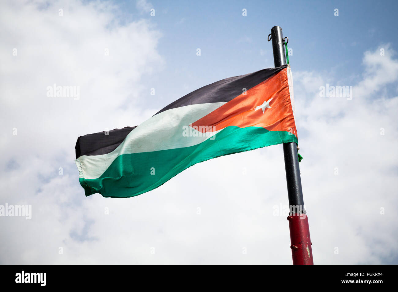 Brandissant le drapeau national de la Jordanie sur le vent sur ciel nuageux Banque D'Images